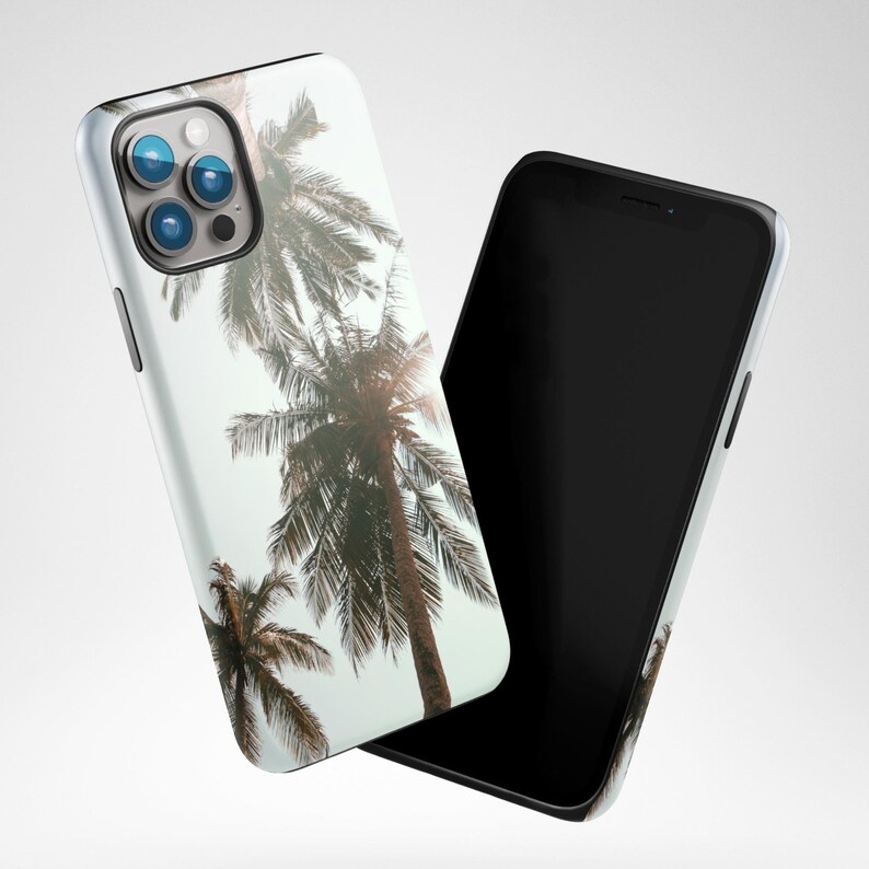 May include: A white phone case with a tropical palm tree design. The case is shown with a black phone.