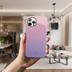 May include: A pink and purple gradient phone case with a camera lens cutout and a small circle logo. The case is made of a smooth, glossy material.