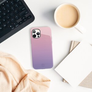 May include: A pink and purple gradient phone case with a clear camera lens cover. The case has a glossy finish and a small logo on the back.