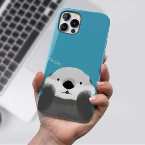 May include: A blue phone case with a cartoon sea otter peeking out from the bottom. The case has a white inscription that says "Smile".