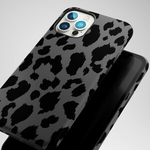 May include: A smartphone case with a gray leopard print design. The case is black and gray with a glossy finish. The phone case is shown with a black smartphone.