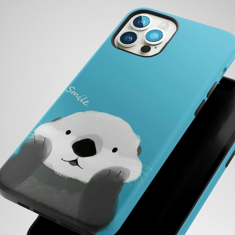 May include: A blue phone case with a cartoon otter holding its paws up to its face and the word "Smile" written on the case.