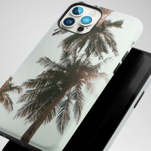 May include: A white iPhone case with a tropical palm tree design. The case has a camera lens cutout with three black camera lenses.