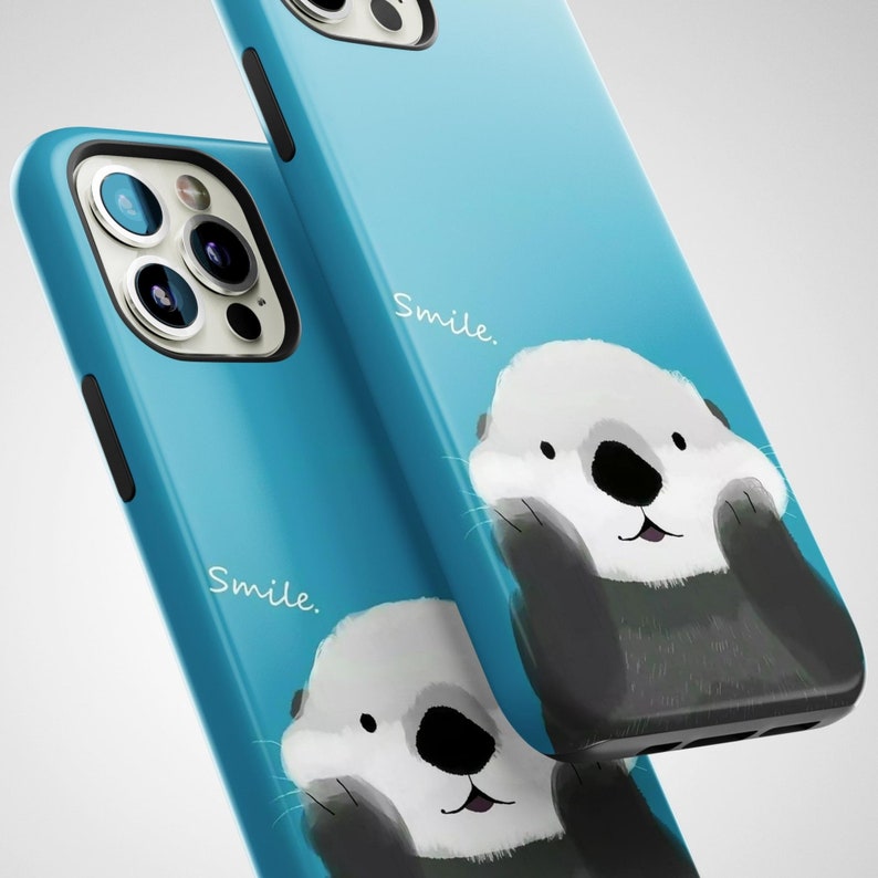 May include: Two blue iPhone cases with a smiling sea otter graphic and the word "Smile." printed on each case.