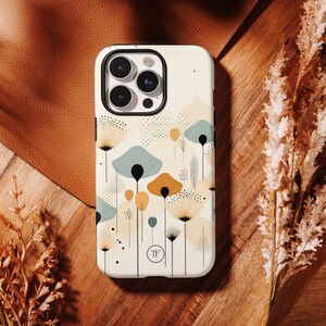 K&ouml;nnte beinhalten: Eine wei&szlig;e iPhone-H&uuml;lle mit einem geometrischen Muster aus abstrakten Blumen in Gelb-, Braun- und Blaut&ouml;nen. Die H&uuml;lle hat ein klares Kameraobjektiv und den Text "TF" in der Mitte.