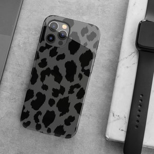 May include: A smartphone case with a gray leopard print design. The case is black and gray with a glossy finish. The phone case is next to a black smartwatch and a laptop.