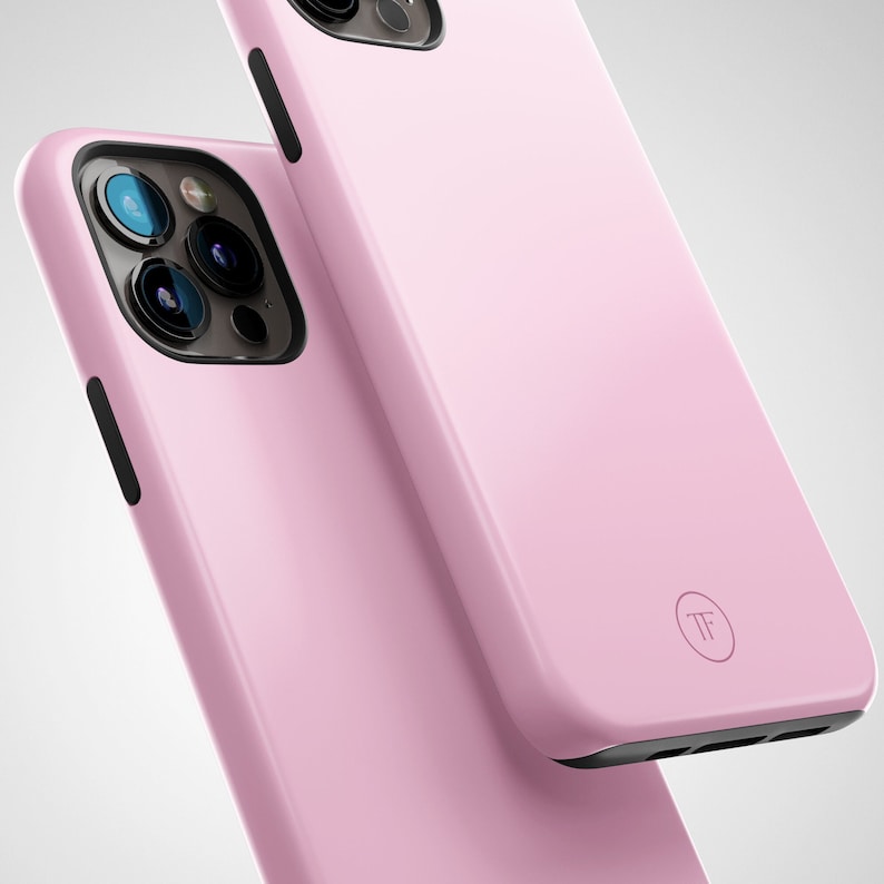 May include: Two pink phone cases with a black camera lens and a black outline. The case on top has a small circle with the letters "TF" inside.
