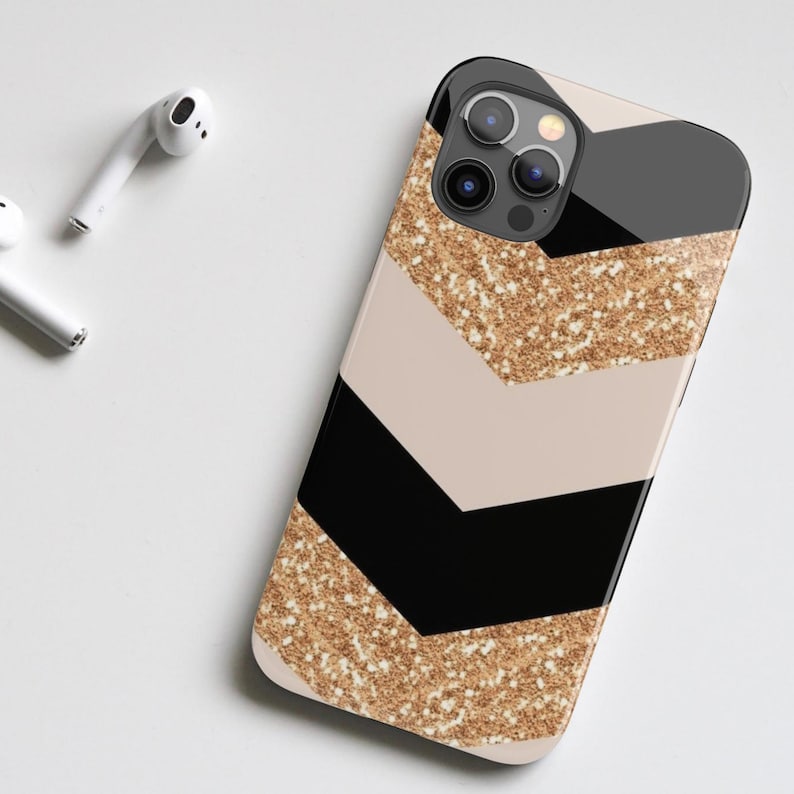 Puede incluir: Una funda para tel&eacute;fono de color negro y beige con un patr&oacute;n de chevron de purpurina dorada. La funda tiene un recorte para el objetivo de la c&aacute;mara.