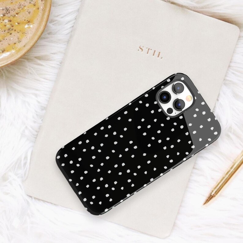 May include: Black phone case with a white polka dot pattern. The case has a camera lens cutout on the back.