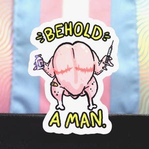 May include: A sticker featuring a cartoon chicken with a syringe and a vial, with the words "BEHOLD A MAN" in yellow. The background includes a transgender pride flag and a wavy pattern.