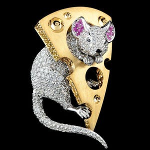 Puede incluir: Una pieza de joyería caprichosa que presenta un ratón saliendo de una cuña de queso. El ratón y el queso están incrustados con gemas brillantes, con gemas rosas para las orejas del ratón. El queso tiene detalles dorados y amarillos.