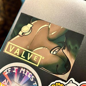 May include: A rectangular sticker featuring a brown, stylized animal character with a small paw print icon and the text VALVE in a yellow box. Below it, a circular sticker with rainbow rays and the text IF I MISS THIS ALL MY MARVELOUS, and a Jollibee sticker.