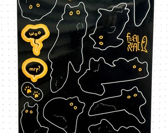 Op de afbeelding: Zwarte stickerpagina met verschillende cartoon kat ontwerpen met gele ogen en tekstballonnen. De tekstballonnen bevatten zinnen als "woo" en "mrp?". De woorden "FERAL REAL" zijn ook aanwezig.