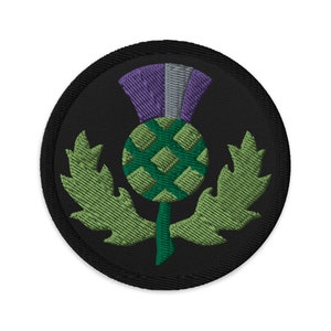 May include: A round black patch with a green and purple embroidered thistle. The thistle has a green stem and leaves.