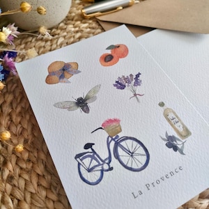 Può includere: Illustrazione ad acquerello su una carta bianca con una bicicletta con un cestino di fiori, un cappello, una falena, lavanda, una pesca e olio d'oliva. Le parole "La Provence" sono stampate sotto.