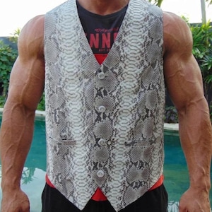May include: A sleeveless waistcoat featuring a grey and white snakeskin pattern with a V-neckline and four light-coloured buttons down the front. The garment includes two small horizontal pockets on the lower front section and has a pointed hemline.