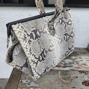 Peut inclure: Un sac &agrave; main en cuir de serpent blanc et gris avec des accents noirs et une poign&eacute;e sup&eacute;rieure.