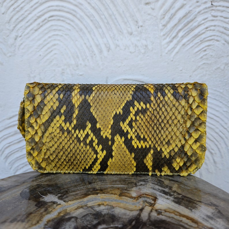 Puede incluir: Un bolso de mano de piel de serpiente amarillo y negro con un patr&oacute;n texturizado.
