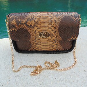 Peut inclure: Une pochette en cuir de serpent brun et beige avec une bandouli&egrave;re en cha&icirc;ne dor&eacute;e et un fermoir dor&eacute;.