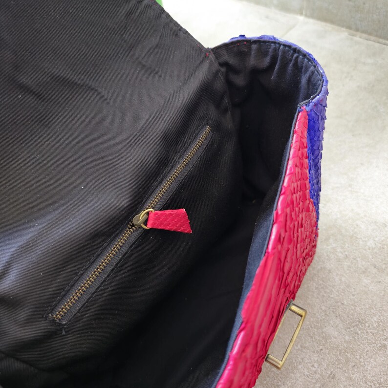 May include: A black fabric-lined handbag with a zipped pocket. The exterior is made of pink, blue, and purple snakeskin.