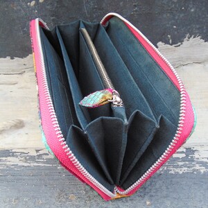 K&ouml;nnte beinhalten: Eine rosa und gr&uuml;n gemusterte Geldb&ouml;rse mit Rei&szlig;verschluss. Die Geldb&ouml;rse ist ge&ouml;ffnet und zeigt mehrere F&auml;cher im Inneren.