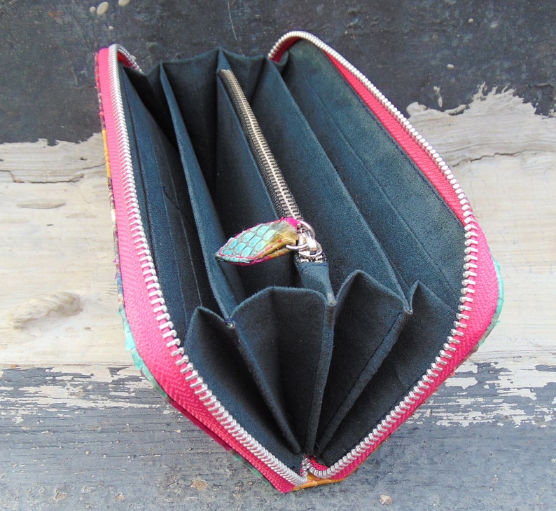 K&ouml;nnte beinhalten: Eine rosa und gr&uuml;n gemusterte Geldb&ouml;rse mit Rei&szlig;verschluss. Die Geldb&ouml;rse ist ge&ouml;ffnet und zeigt mehrere F&auml;cher im Inneren.