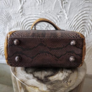 May include: A brown snakeskin handbag with gold accents and four metal feet on the bottom.