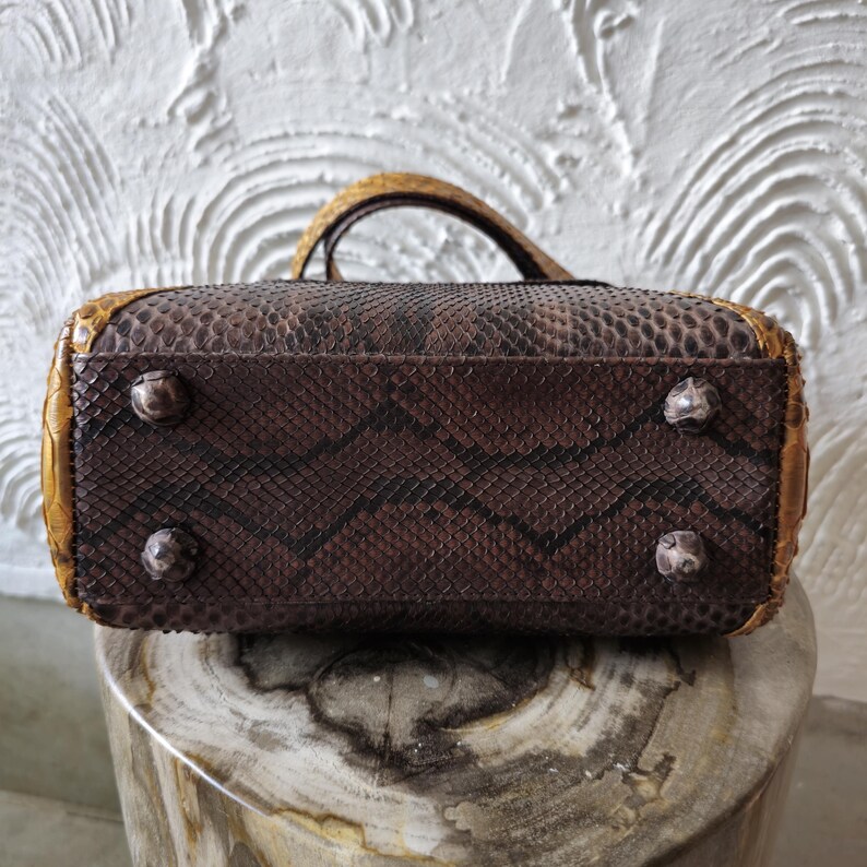 May include: A brown snakeskin handbag with gold accents and four metal feet on the bottom.