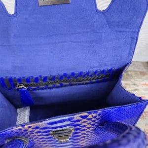 Pu&ograve; includere: Borsa a mano in pelle di serpente blu con una tasca con cerniera e una chiusura argentata. La borsa &egrave; foderata in tessuto blu.