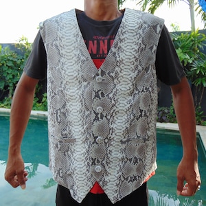 May include: A white and gray snakeskin vest with a button-up front. The vest has a V-neck and two pockets on the sides.