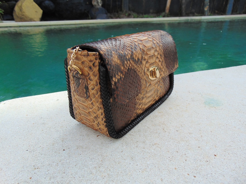 Peut inclure: Un petit sac &agrave; main en cuir de serpent brun et beige avec une bandouli&egrave;re tress&eacute;e noire et un fermoir dor&eacute;.