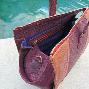 May include: A burgundy, brown, and orange snakeskin handbag with a red zipper and gold hardware. The bag is open and the interior is lined with blue fabric.