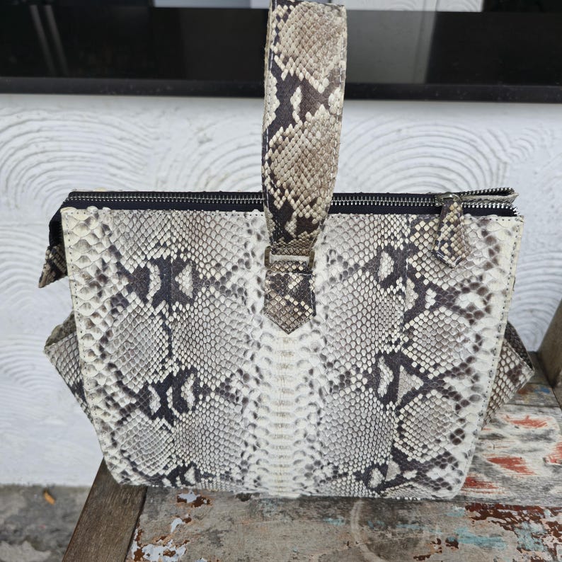 Peut inclure: Un sac &agrave; main en cuir de serpent blanc et noir avec une fermeture &eacute;clair et une poign&eacute;e sup&eacute;rieure en cuir de serpent.