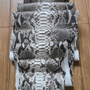 以下が含まれることがあります： グレー、黒、白の色合いの、積み重ねられたなめし革のヘビ革。 爬虫類の革の自然な模様と質感を表現するために、革は垂直に積み重ねられています。 木の表面にあります。