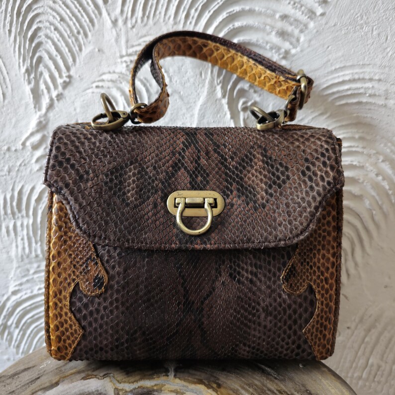 May include: A brown and tan snakeskin handbag with a gold clasp and a detachable strap.