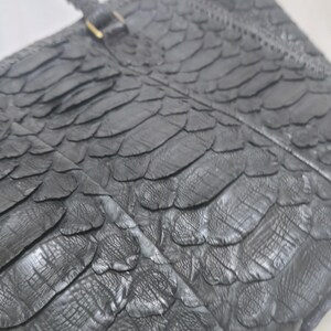 May include: A black leather handbag with a textured, scale-like pattern. The bag features a braided handle and a gold-coloured clasp. The design is sleek and sophisticated, suitable for various occasions.