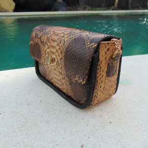 Peut inclure: Un petit sac &agrave; main en cuir de serpent brun et noir avec un fermoir dor&eacute; et une fermeture &eacute;clair.