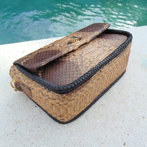 Peut inclure: Un sac &agrave; main en cuir de serpent brun avec une bordure tress&eacute;e noire et un fermoir dor&eacute;.