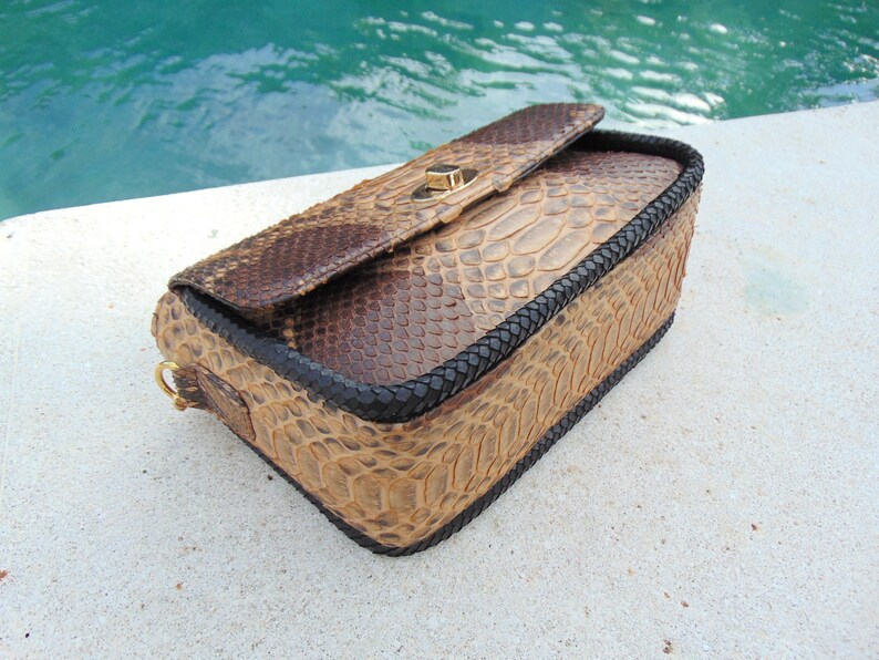 Peut inclure: Un sac &agrave; main en cuir de serpent brun avec une bordure tress&eacute;e noire et un fermoir dor&eacute;.