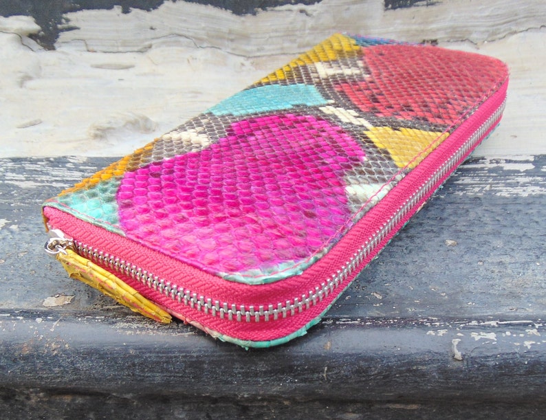 K&ouml;nnte beinhalten: Eine farbenfrohe Schlangenleder-Geldb&ouml;rse mit einem pink-, gelb-, blau- und gr&uuml;nen Muster. Die Geldb&ouml;rse hat einen Rei&szlig;verschluss.