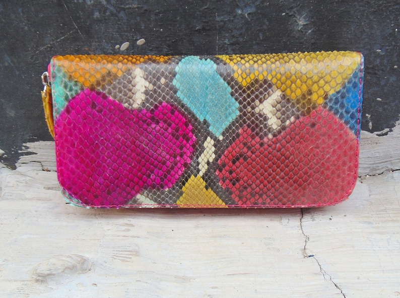 K&ouml;nnte beinhalten: Eine farbenfrohe Schlangenleder-Geldb&ouml;rse mit einem geometrischen Muster in den Farben Pink, Rot, Gelb, Blau und Wei&szlig;.