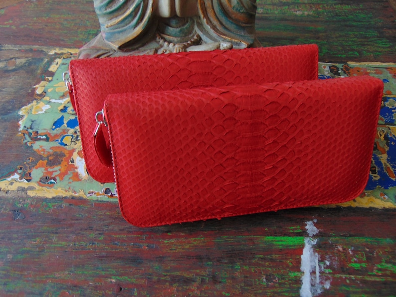 May include: Two red leather wallets with a snakeskin pattern and zipper closures.