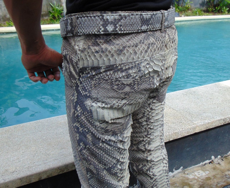 K&ouml;nnte beinhalten: Nahaufnahme einer Hose aus Schlangenhaut mit passendem G&uuml;rtel. Die Hose ist eine Mischung aus Grau, Schwarz und Wei&szlig; mit einem strukturierten, schuppigen Muster. Der G&uuml;rtel hat ein &auml;hnliches Design. Die Hose wird von einer Person getragen.