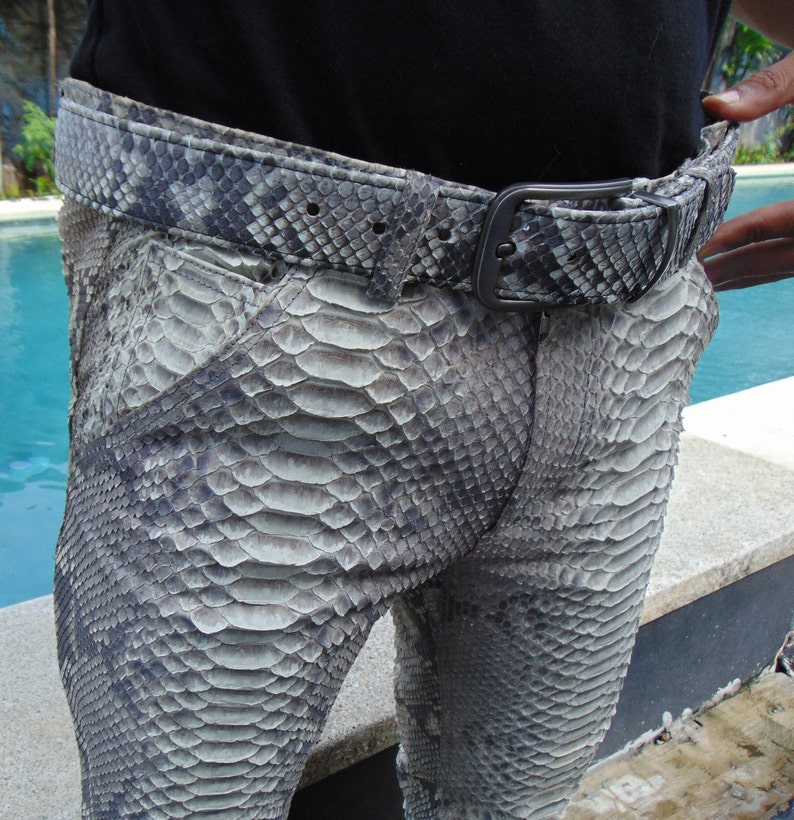 K&ouml;nnte beinhalten: Eine Hose in Grau und Wei&szlig; mit Schlangenmuster und passendem G&uuml;rtel. Der G&uuml;rtel hat eine dunkle Metallschnalle. Die Hose besteht aus einem Material, das die Textur von Schlangenhaut nachahmt.
