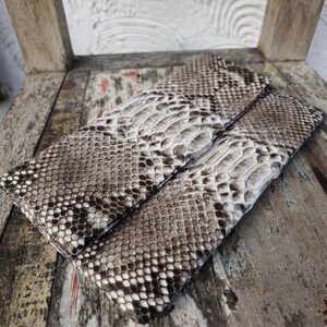 May include: A clutch purse made of brown and white snakeskin. The purse has a fold-over closure and a textured surface.