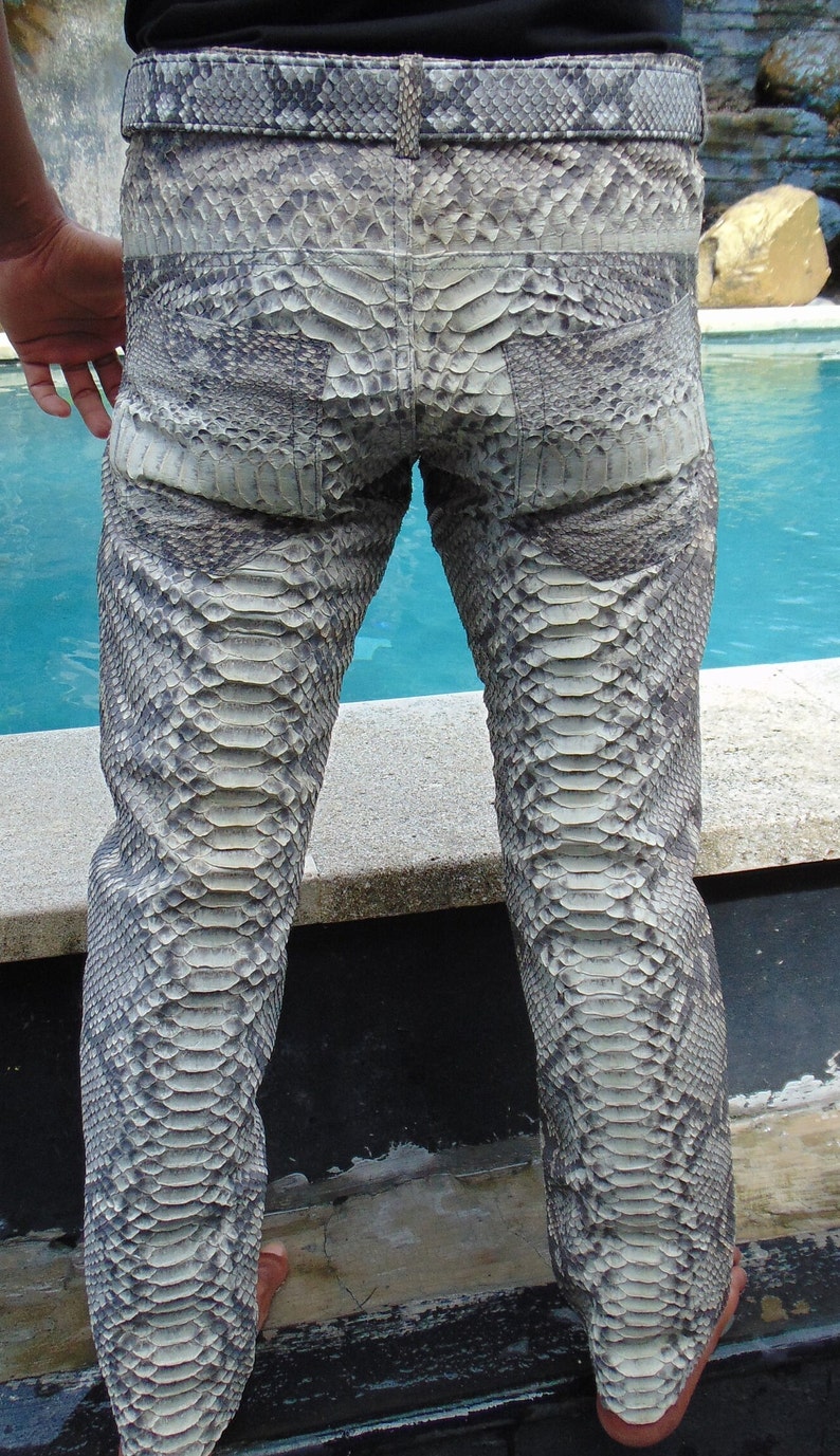 K&ouml;nnte beinhalten: Eine Hose aus grau-wei&szlig;em Schlangenhaut. Die Hose hat einen G&uuml;rtel und Taschen. Das Schlangenhautmuster ist auf der gesamten Hose sichtbar. Die Hose wird von einer Person getragen, die sich in der N&auml;he eines Pools befindet.