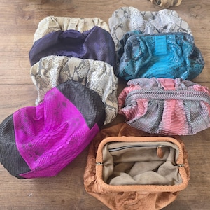 Puede incluir: Una colección de ocho bolsos de mano con diversas texturas y colores, incluyendo patrones de piel de serpiente en beige, gris y azul, un bolso morado sólido, un bolso rosa brillante y negro, un bolso rosa y gris, y un bolso beige abierto con cremallera.