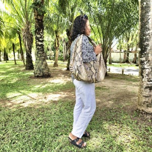 May include: A woman is carrying a large, brown and black snakeskin handbag with a hobo style design. The bag is worn over her shoulder and she is standing in a tropical setting.