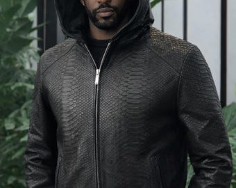May include: A black hooded jacket featuring a textured snakeskin pattern throughout the exterior. The garment includes a full-length silver-toned metal zip closure down the centre front and two side pockets with matching silver-toned zip hardware.