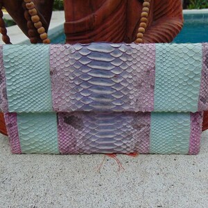 Pu&ograve; includere: Una pochette in pelle di serpente blu chiaro e viola con chiusura a lembo.